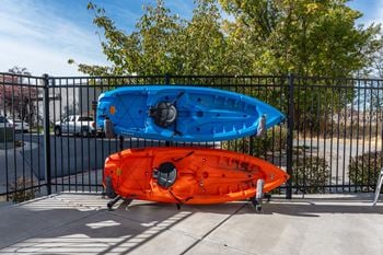 Two kayaks, one blue and one orange, are on wheels and leaning against a black fence